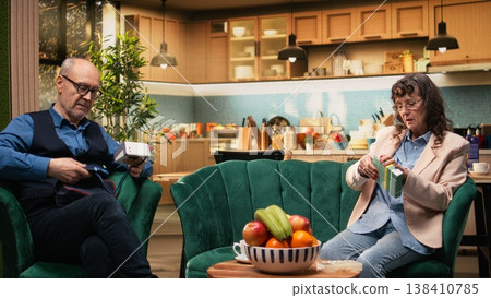 Aged woman checking prescribed pills box and man preparing BP monitor, senior couple with daily healthcare on couch. In-home healthcare, disease management and routine supports longevity. 138410785