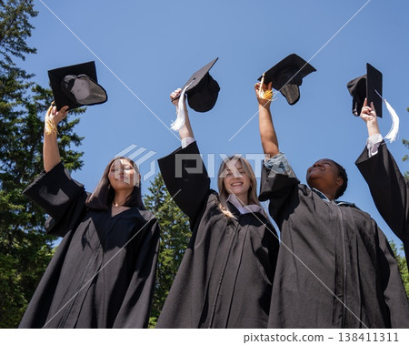 Young women of different nationalities pull graduation caps up. Young women of different nationalities pull graduation caps up. 138411311