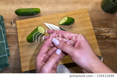 A close-up of a finger cut on the hand with a knife against the background of a cutting board, cucumbers, and a knife in the kitchen. High quality photo 138412690