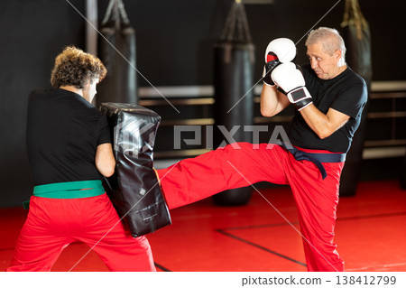 Senior man firing front kick at shield during Krav Maga drill 138412799