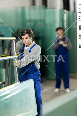 Man glazer employee in blue overall works in glass processing shop 138412804