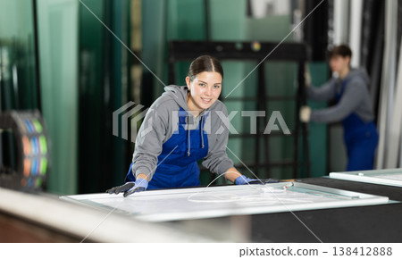 Girl glazer employee in blue overall works in glass processing shop Girl glazer employee in blue overall works in glass processing shop 138412888