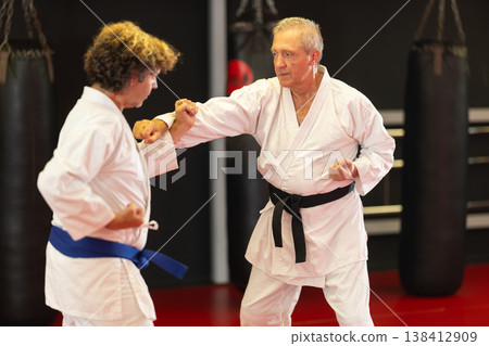 Older karate fighter practicing paired kumite in dojo Older karate fighter practicing paired kumite in dojo 138412909