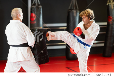 Man in white kimono practices punching with trainer 138412931