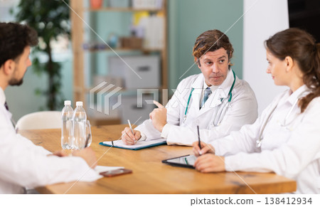 Representatives of medical professional community sitting at table and chatting Representatives of medical professional community sitting at table and chatting 138412934