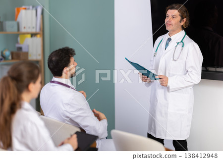 Male medical lecturer with folder addressed to attendees lecture Male medical lecturer with folder addressed to attendees lecture 138412948