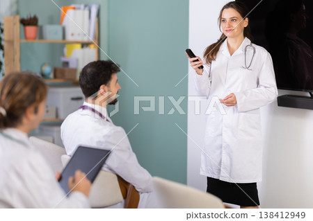 Female doctor lecturer communicates and addressed to attendees, control projector using remote control Female doctor lecturer communicates and addressed to attendees, control projector using remote control 138412949