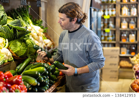 Man diligently picking out zucchini to buy in vegetable aisle of supermarket 138412953