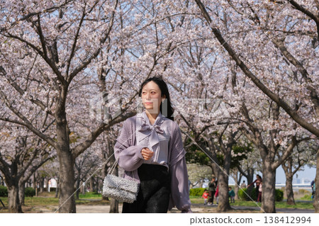 Young woman walking under a cherry blossom tree in full bloom Young woman walking under a cherry blossom tree in full bloom 138412994