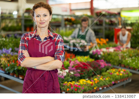Middle-aged saleswoman standing against the background of various flowers 138413007
