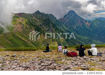 A view of the Yatsugatake mountain range, specifically the summit of Mt. Iou, with climbers and the surrounding mountains of Mt. Yokodake and Mt. Akadake. 138413032