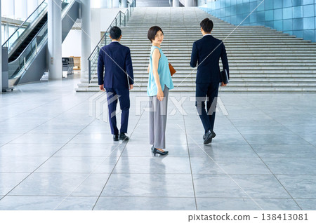 一個商務團隊走過辦公大樓大廳,一位女士微笑地轉過身來。 一個商務團隊走過辦公大樓大廳,一位女士微笑地轉過身來。 138413081