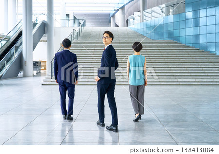 一個商務團隊走向辦公大樓的樓梯，一個微笑的男人轉過身來。 138413084