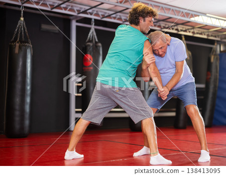 Mature man and adult man practice self-defense techniques at gym Mature man and adult man practice self-defense techniques at gym 138413095