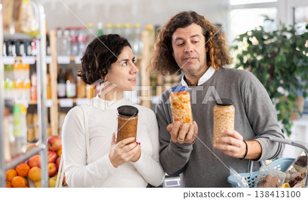 In store, couple near counter are looking at canned beans and lentils In store, couple near counter are looking at canned beans and lentils 138413100