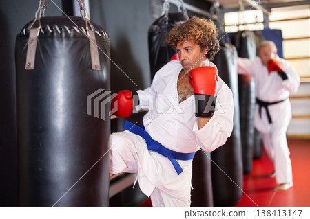 Man in white kimono practices punching punching bag Man in white kimono practices punching punching bag 138413147