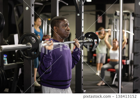 African man doing squats with weight using half rack in gym African man doing squats with weight using half rack in gym 138413152