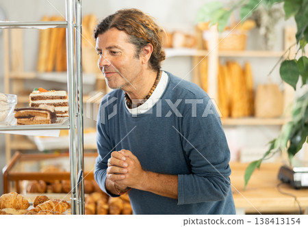 Man in casual clothes chooses fresh cake for breakfast in bakery Man in casual clothes chooses fresh cake for breakfast in bakery 138413154