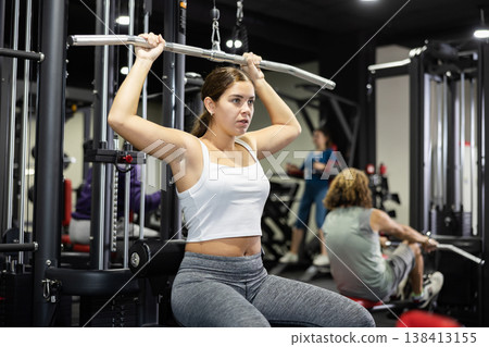 Caucasian woman doing exercises on lat pull down machine in gym 138413155