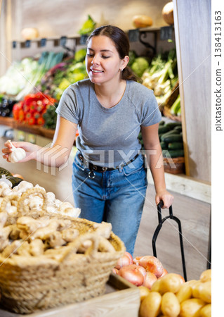 Female shopper examines and chooses ripe garlic on grocery store shelves Female shopper examines and chooses ripe garlic on grocery store shelves 138413163