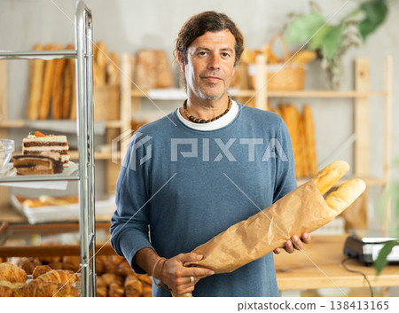 Pleased middle-aged guy holding baguettes in paper bag in bakery 138413165
