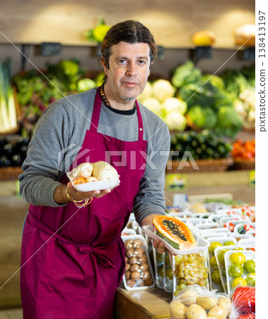 Male grocery store worker offers various packaged ripe fruits and vegetables Male grocery store worker offers various packaged ripe fruits and vegetables 138413197