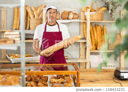Male baker placing fresh baguettes in paper bag for customer Male baker placing fresh baguettes in paper bag for customer 138413231
