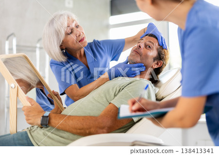 Man looking at mirror while female cosmetologist showing results of facial procedure 138413341