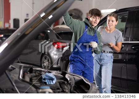 Auto technician explaining required car engine maintenance to female customer 138413346