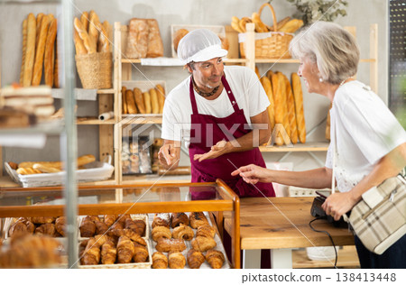 Man owner of bakery serves elderly female visitor, communicates with client 138413448