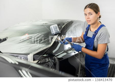 Young woman mechanic paints car with machine Young woman mechanic paints car with machine 138413470