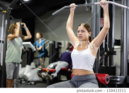 Caucasian woman training on lat pull down machine in gym Caucasian woman training on lat pull down machine in gym 138413511
