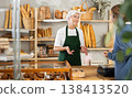 Elderly woman owner of bakery serves male visitor, communicates with client 138413520