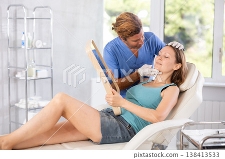 Adult male doctor examining face of female patient Adult male doctor examining face of female patient 138413533