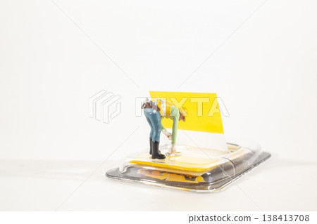 Miniature worker bending over bright yellow packaging Miniature worker bending over bright yellow packaging 138413708