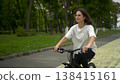 Young woman in white t shirt and black leggings riding bicycle in park front view. 4k 138415161