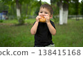 Three year old boy eats cheeseburger outdoors and looks at camera portrait 4k 138415168