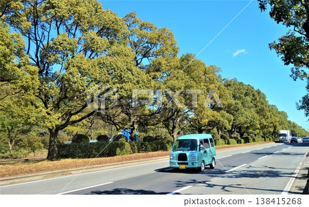 一輛時尚的藍色汽車行駛在綠樹成蔭的道路上。 一輛時尚的藍色汽車行駛在綠樹成蔭的道路上。 138415268