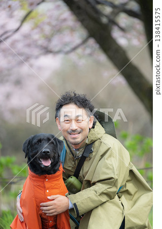 A dog and its owner wearing raincoats: A heartwarming spring walk scene of a man and his dog in the rain, capturing the feeling of nature. A dog and its owner wearing raincoats: A heartwarming spring walk scene of a man and his dog in the rain, capturing the feeling of nature. 138415575