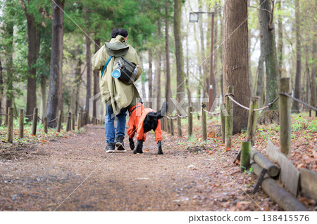 Dog and owner wearing an incoat; full-body shot of a man walking a large dog in the rain (faceless, from behind). Dog and owner wearing an incoat; full-body shot of a man walking a large dog in the rain (faceless, from behind). 138415576