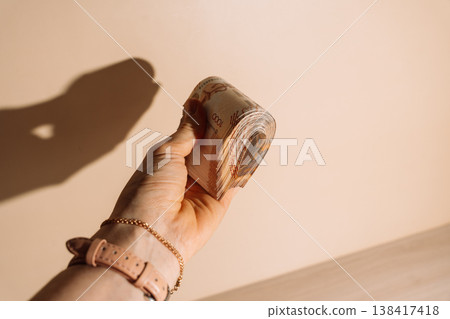 Close up hand holding a roll of Kazakhstani tenge banknotes on beige background with hard shadow, cash concept Close up hand holding a roll of Kazakhstani tenge banknotes on beige background with hard shadow, cash concept 138417418