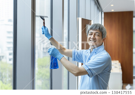 A senior male cleaning staff member smiles and looks directly at the camera. A senior male cleaning staff member smiles and looks directly at the camera. 138417555