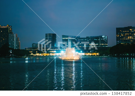 Illuminated fountain on lake in Benchakitti Park with Bangkok skyline view, Night cityscape with glowing pond fountain and reflections near QSNCC Benjakitti Illuminated fountain on lake in Benchakitti Park with Bangkok skyline view, Night cityscape with glowing pond fountain and reflections near QSNCC Benjakitti 138417852