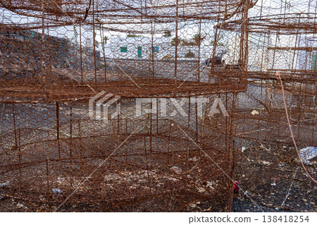 An eye-level shot of old, rusty fish traps situated outdoors, near a coastal community. The aged metal cages suggest a history of maritime work. An eye-level shot of old, rusty fish traps situated outdoors, near a coastal community. The aged metal cages suggest a history of maritime work. 138418254