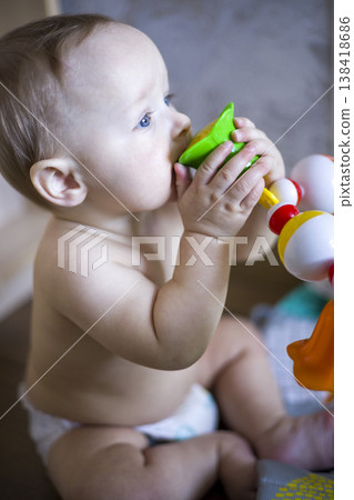Caucasian Baby Chewing Bright Green Teether With Focused Gaze, Sitting In Diaper On Floor, Sensory Exploration And Teething Relief Captured In Candid Close Shot verical Caucasian Baby Chewing Bright Green Teether With Focused Gaze, Sitting In Diaper On Floor, Sensory Exploration And Teething Relief Captured In Candid Close Shot verical 138418686