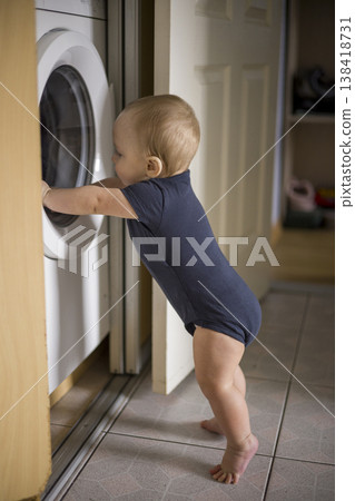 Inquisitive Child Exploring. Toddler Engaging With Washing Machine. Young Child Reaching Into Laundry Drum Playfully. Baby In Navy Outfit Exploring Laundry Area Happily verical Inquisitive Child Exploring. Toddler Engaging With Washing Machine. Young Child Reaching Into Laundry Drum Playfully. Baby In Navy Outfit Exploring Laundry Area Happily verical 138418731