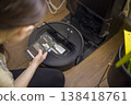 Woman Checks Robot. Inspecting Vacuum With Smartphone. Homeowner Examines Robot Vacuum Using App. Person Troubleshooting Robotic Cleaner With Device And App Insights 138418761
