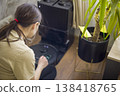 Woman Using App To Control Robot. Woman Operates Robotic Cleaner Via Application Interface. Female User Adjusts Device Settings With Smartphone Near Docking Station 138418765