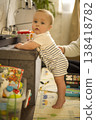 Infant Practices Standing With Support In Playful Home Setting. Caucasian Infant Working On Balancing Skills With Attentive Adult Supervision In Secure Playroom verical 138418782