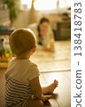 Caucasian Baby Sitting On Floor Watching Blurred Caregiver In Background, Warm Backlit Scene, Reflective Pause, Domestic Playroom Mood And Family Connection verical 138418783
